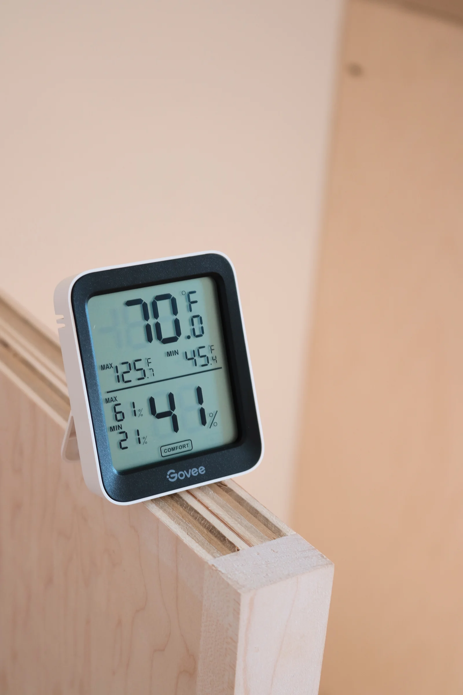 Indoor temperature and humidity monitor resting on natural wood cabinetry