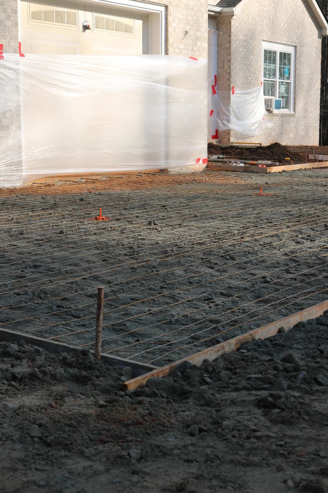 Steel reinforcement laid out before a concrete pour beside a brick home